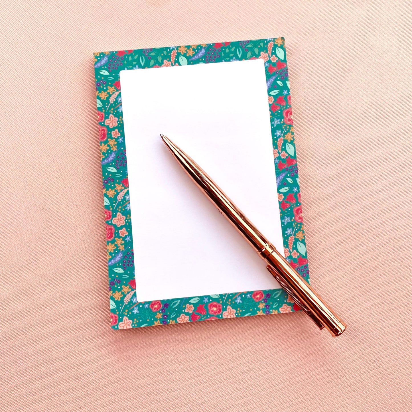 Floral notepad with a pen on a pink background