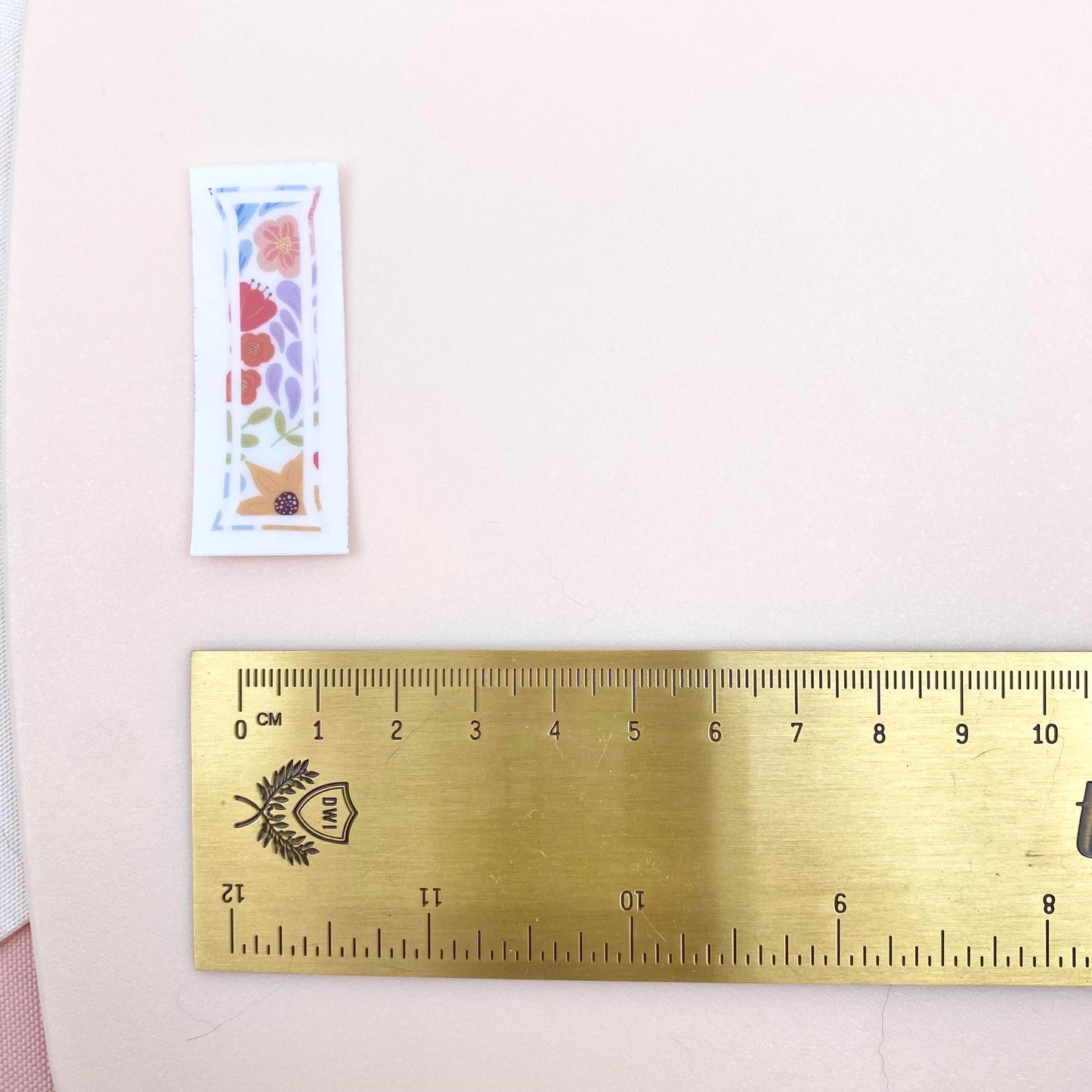 A floral-patterned letter 'I' sticker against a white background with a gold ruler for scale.