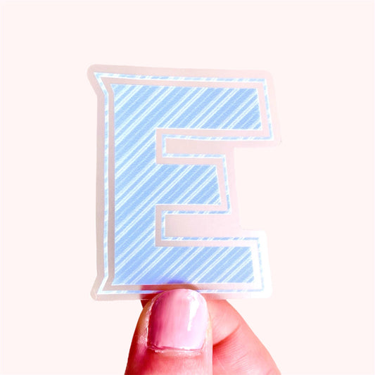 Sticker with a blue and white striped letter 'E' held by a hand on a white background