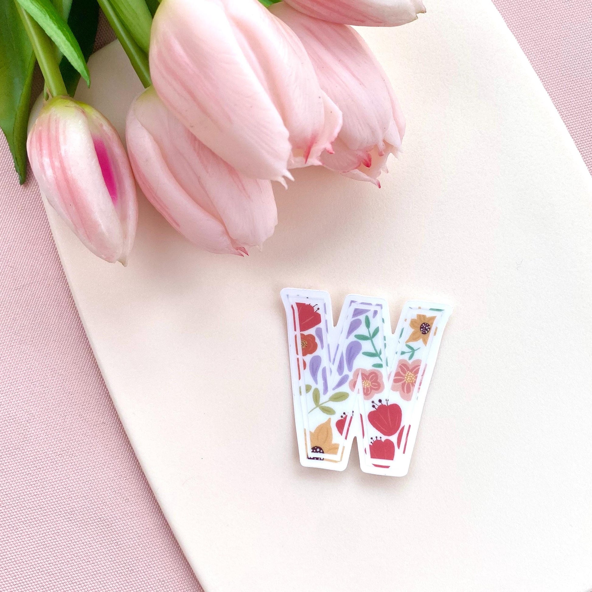 Letter 'W' sticker with floral design on a pink surface with tulips