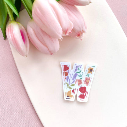 Letter 'W' sticker with floral design on a pink surface with tulips