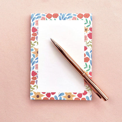 Floral-patterned notepad with a rose gold pen on a pink background