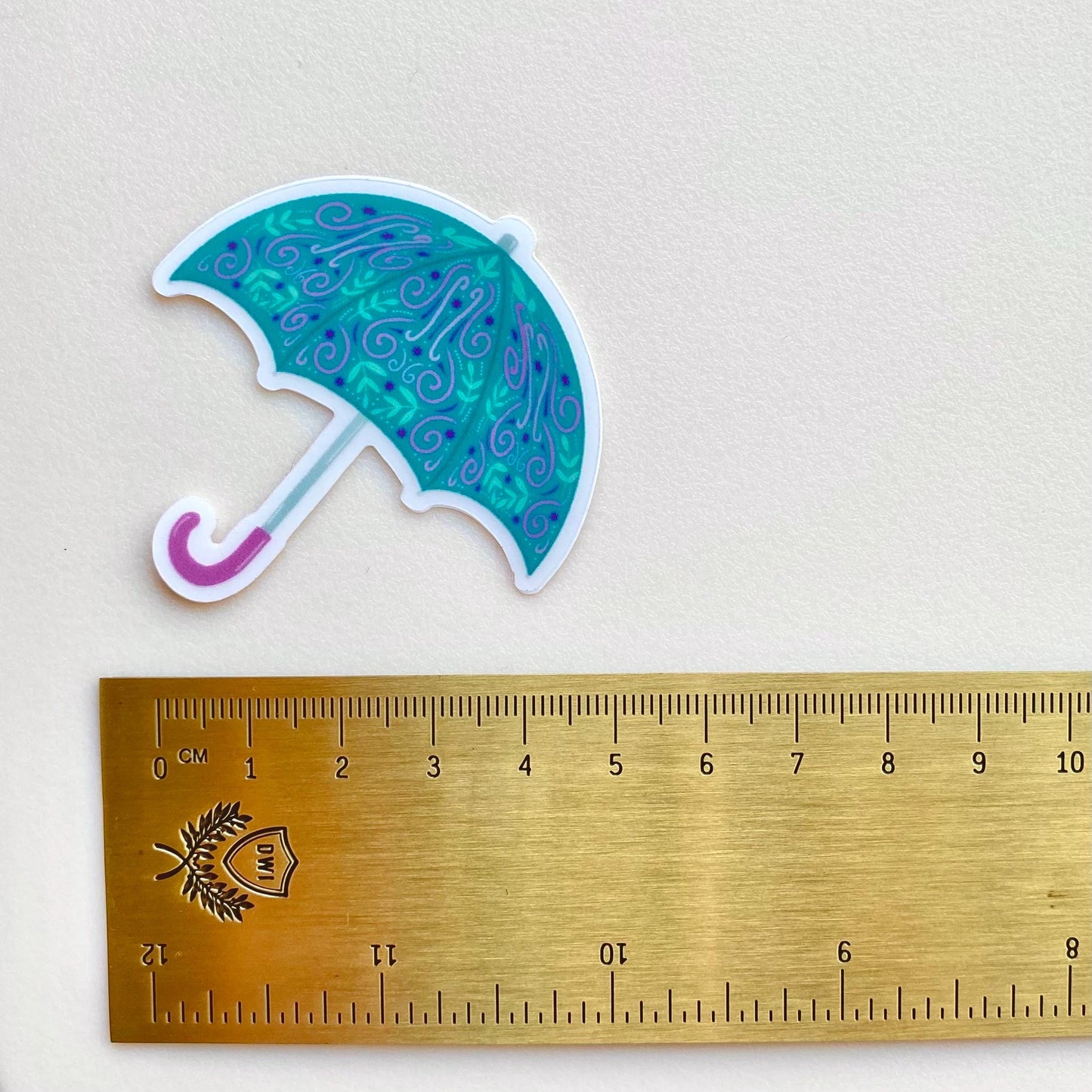 Umbrella-shaped sticker with decorative pattern next to a ruler on a light gray background