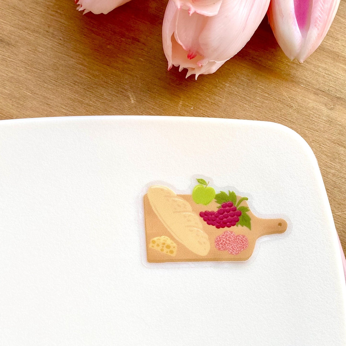 Charcuterie board sticker with a baguette, cheese, grapes, apple and salami, against a cream background