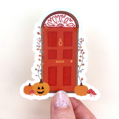 Decorative Halloween door sticker with pumpkins and a red door held by hand against a white background