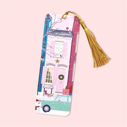 Decorative bookmark depicting a wintery street scene with pink houses with gold tassel on a pink background
