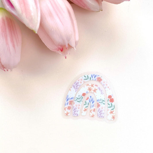 Decorative rainbow-shaped sticker with floral design on a light pink background with tulips.