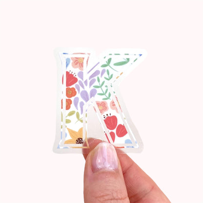 Floral-patterned letter 'K' sticker held by a hand on a white background