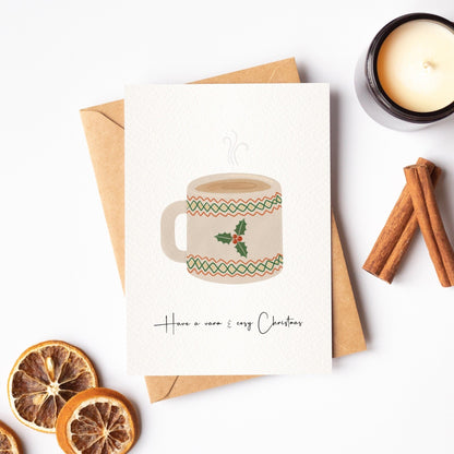 Christmas card with a mug illustration, cinnamon sticks, dried oranges, and a candle on a white background.