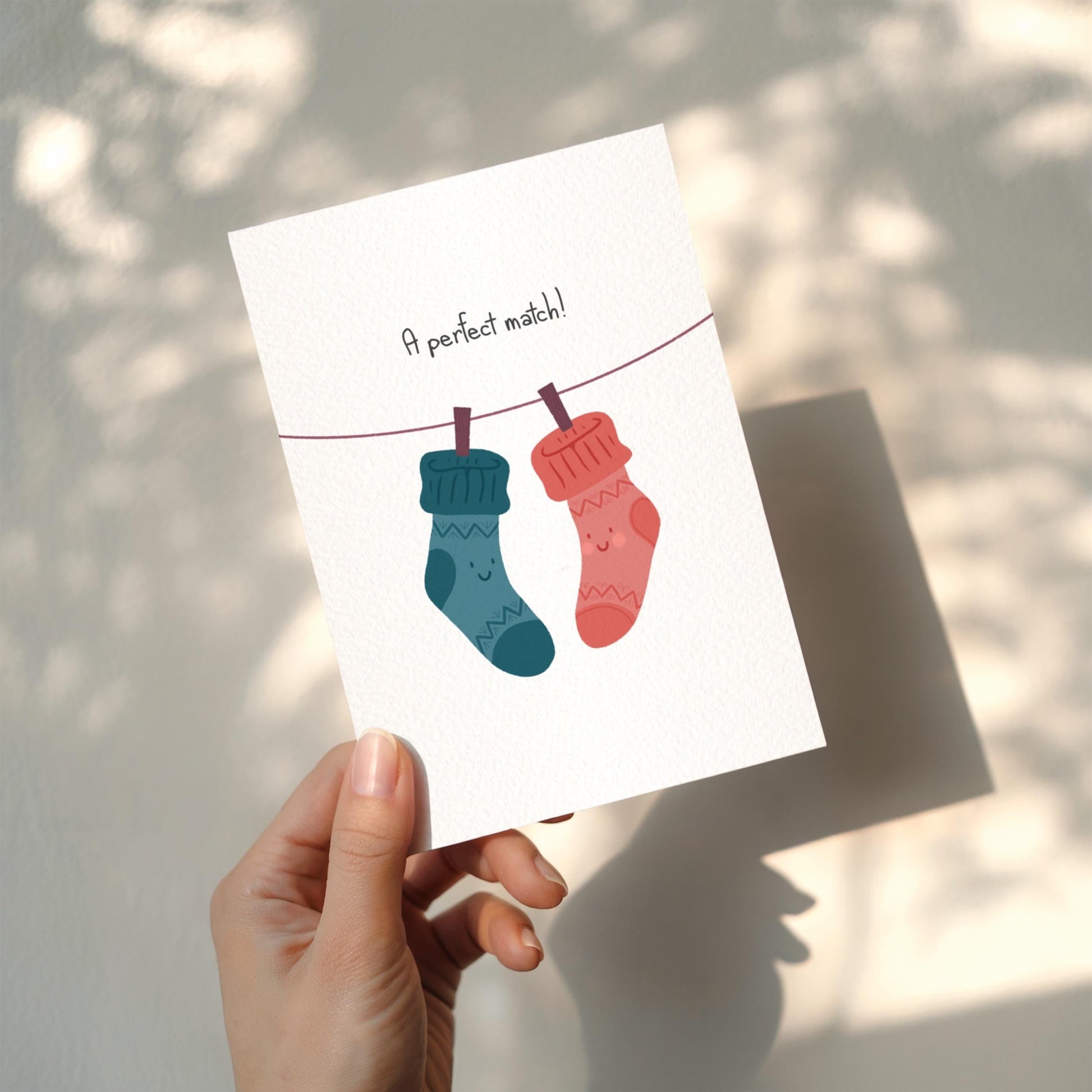 Card with two socks on a line and text 'A perfect match!' held by a hand.