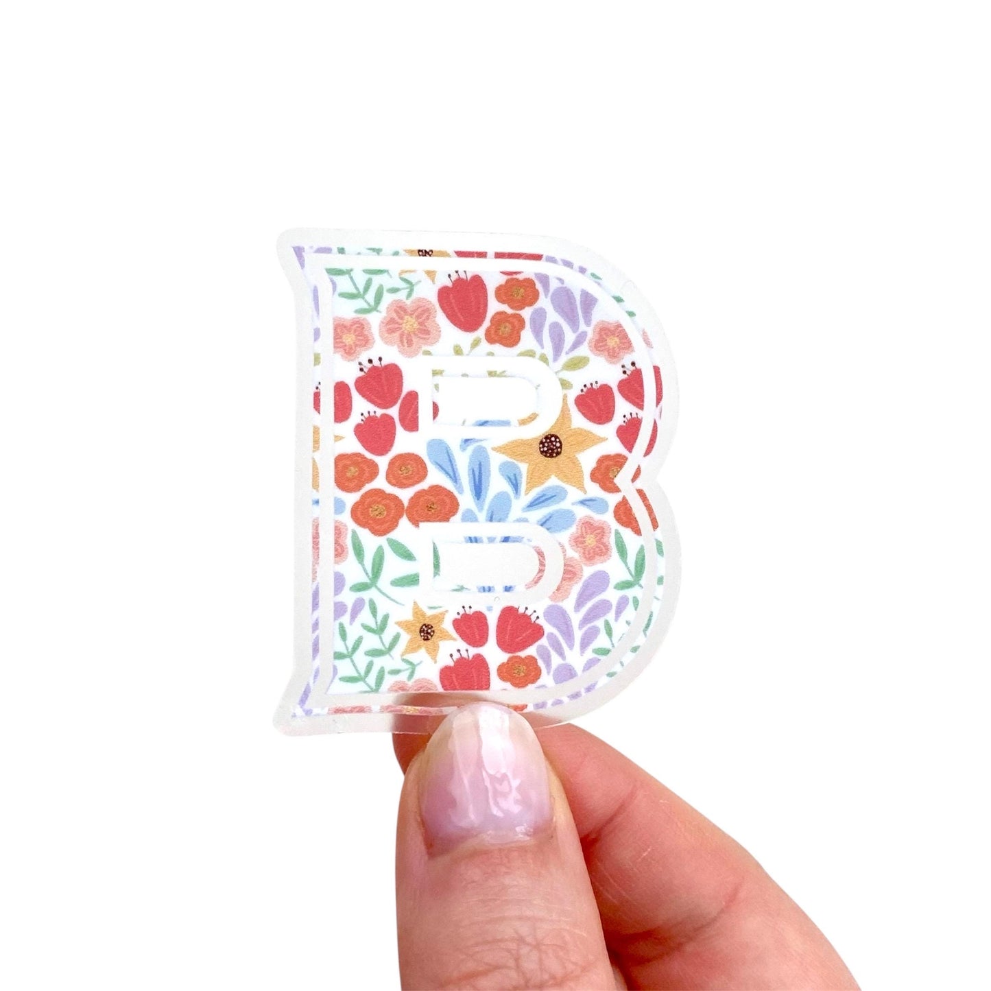 Hand holding a floral letter 'B' sticker against a white background