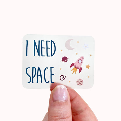 Transparent sticker with 'I Need Space' text and space-themed illustrations held by a hand