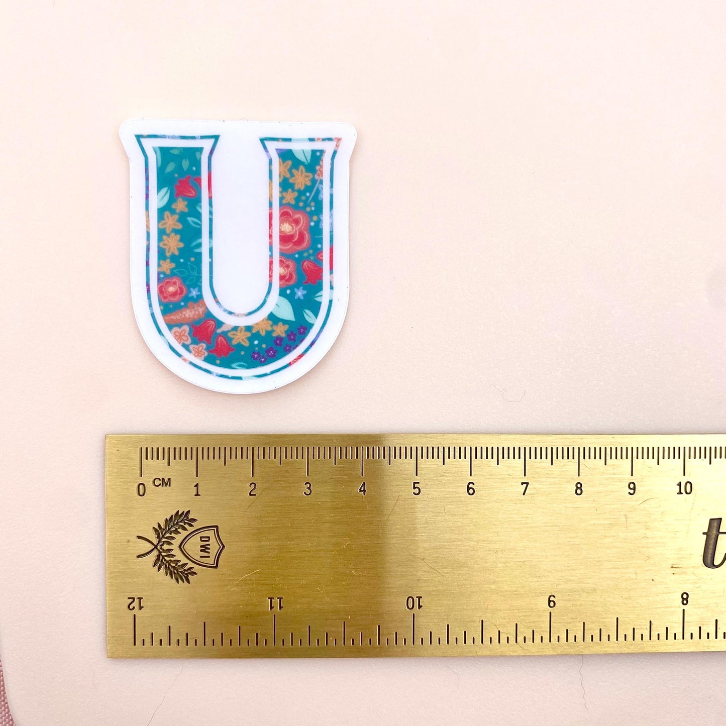 Floral letter 'U' sticker on a beige background with a ruler for scale.