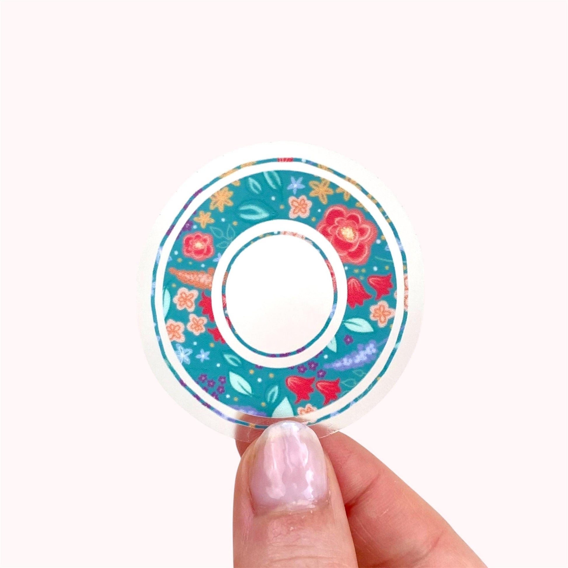 Decorative letter 'O' sticker with floral pattern held by a hand on a white background