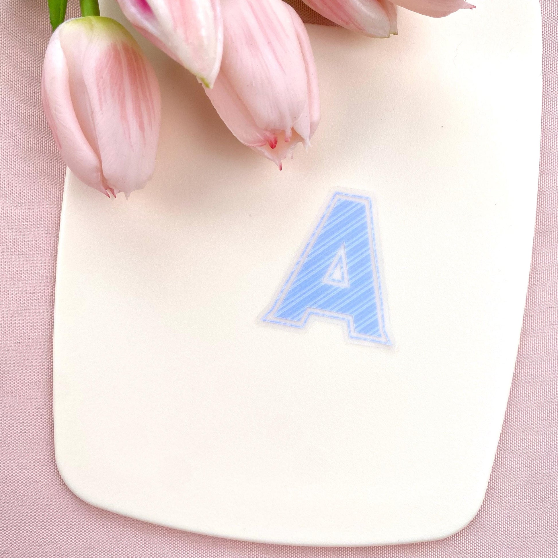 A blue striped letter 'A' sticker against a white background with pink tulips