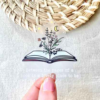 Hand holding a clear book sticker with floral design and quote, woven mat in background