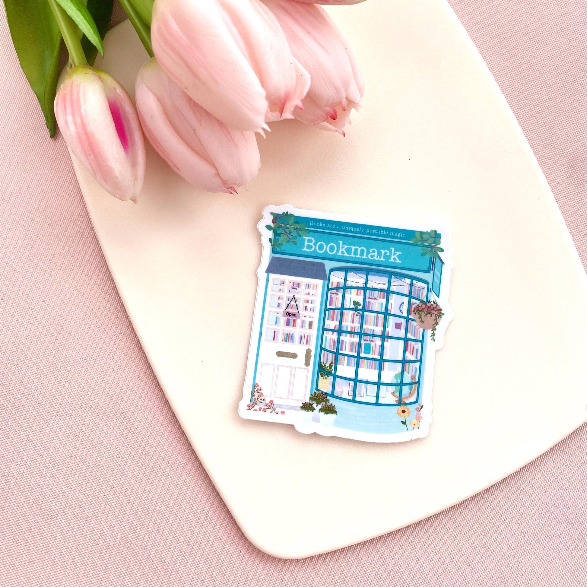 Sticker with a teal blue bookshop design on a pink surface with tulips