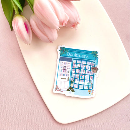 Sticker with a teal blue bookshop design on a pink surface with tulips