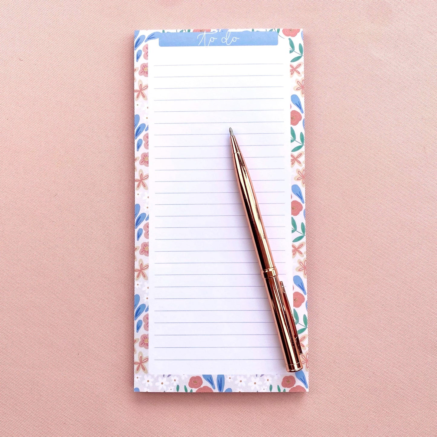 Notepad with floral border and pen on a pink background