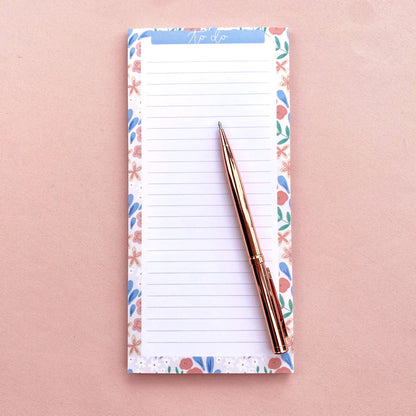 Notepad with floral border and pen on a pink background