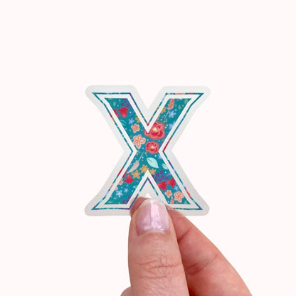 Decorative letter 'X' sticker held by a hand on a white background