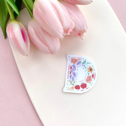 Decorative letter 'D' sticker with floral design on a white surface with pink tulips.