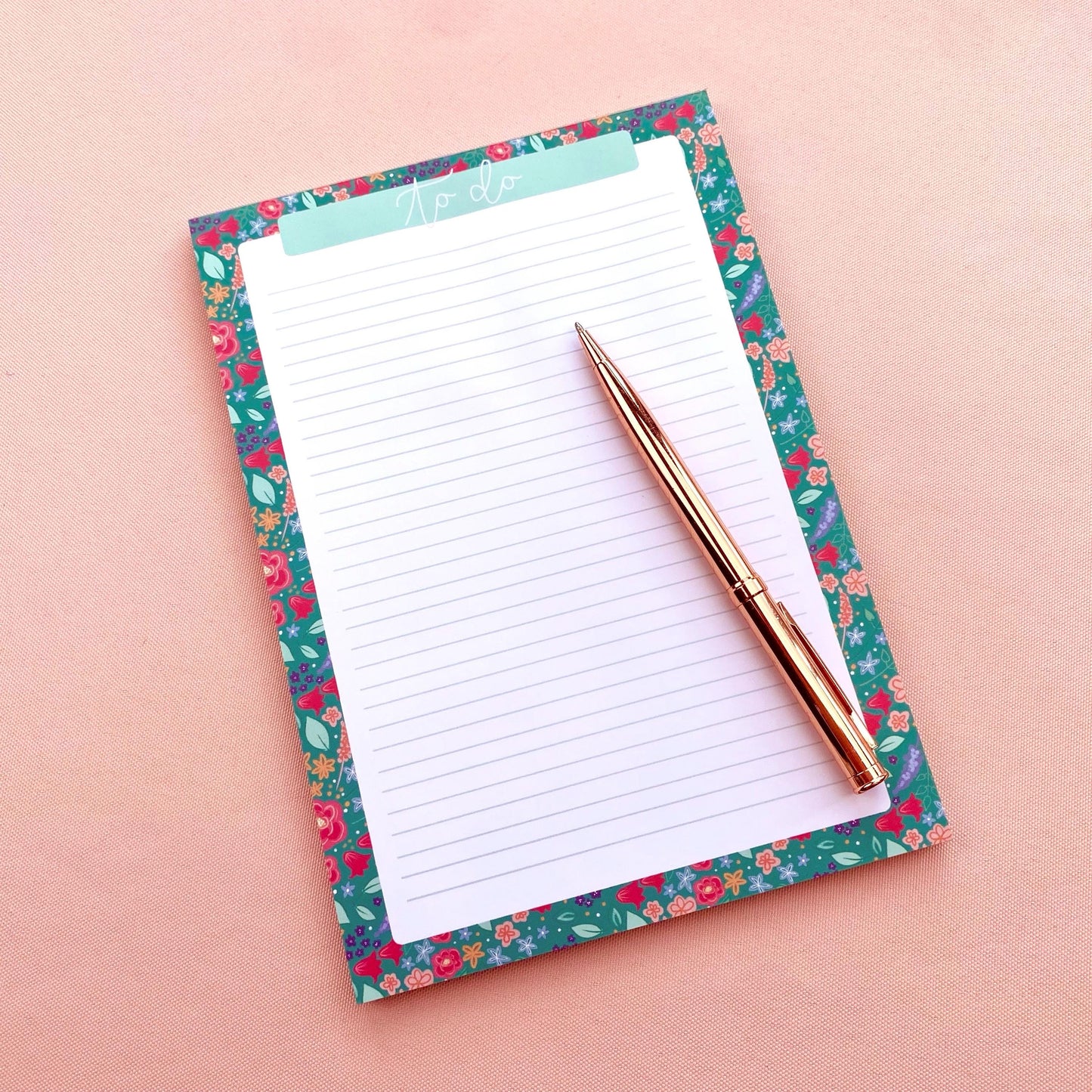 Floral notepad with a pen on a pink background