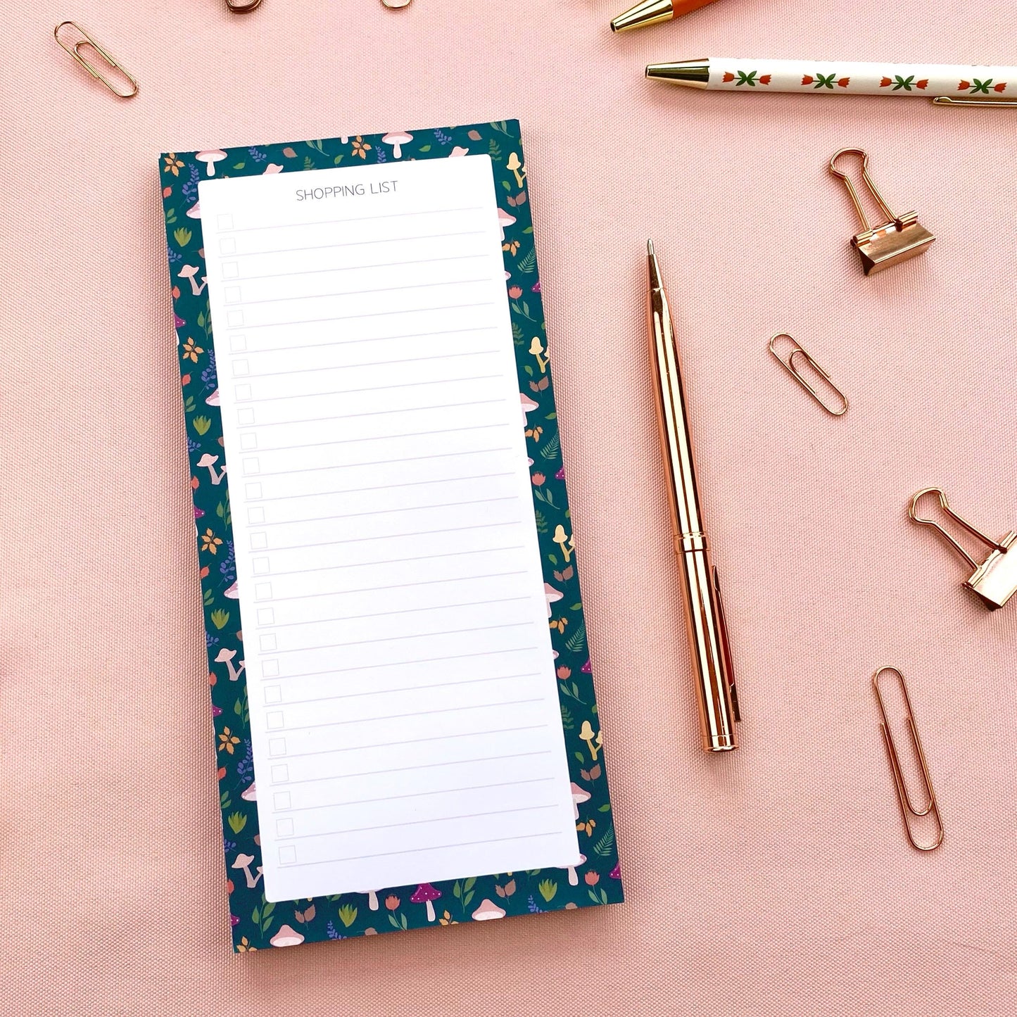 Slim shopping list notepad with autumn foliage border on a pink background with stationery items