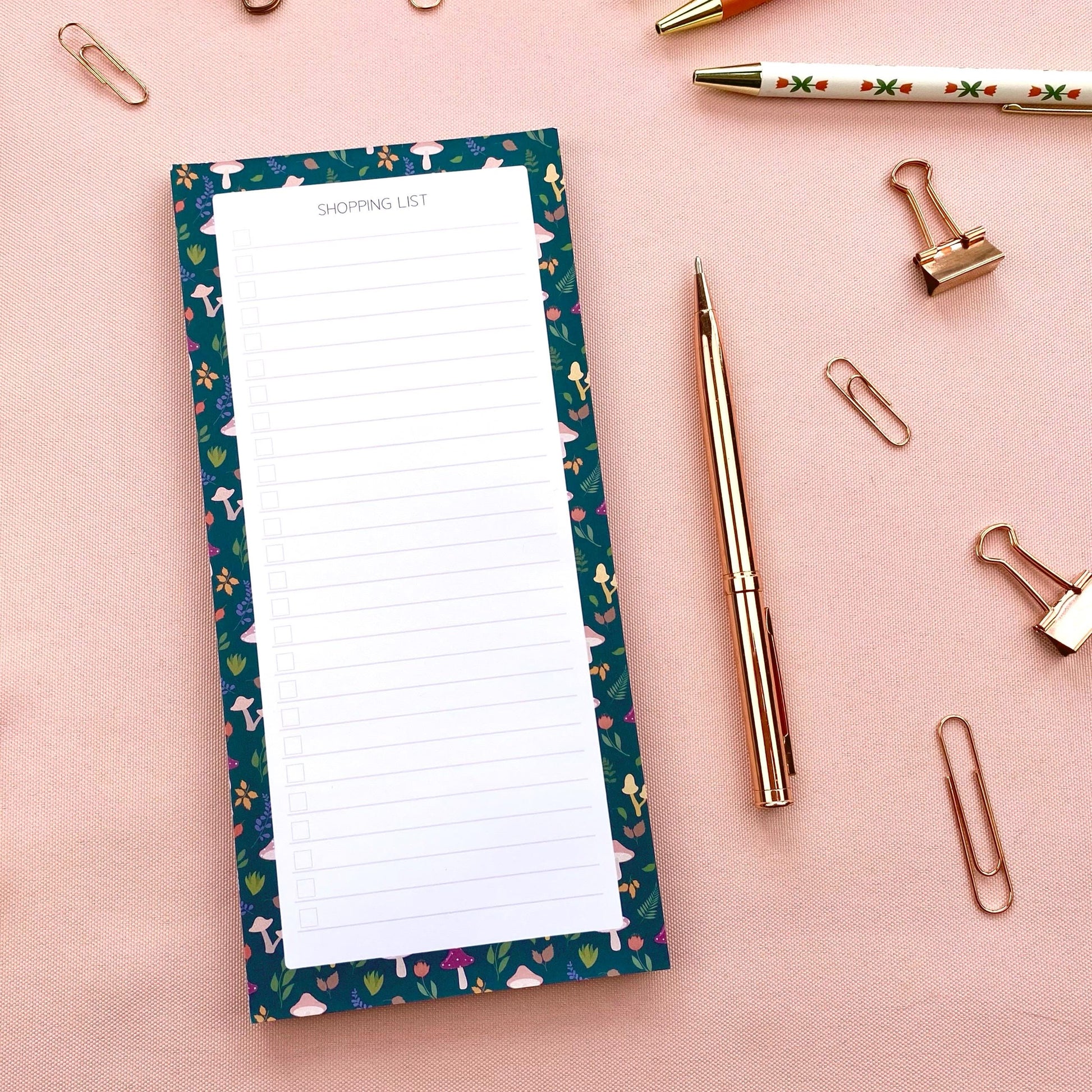 Slim shopping list notepad with autumn foliage border on a pink background with stationery items