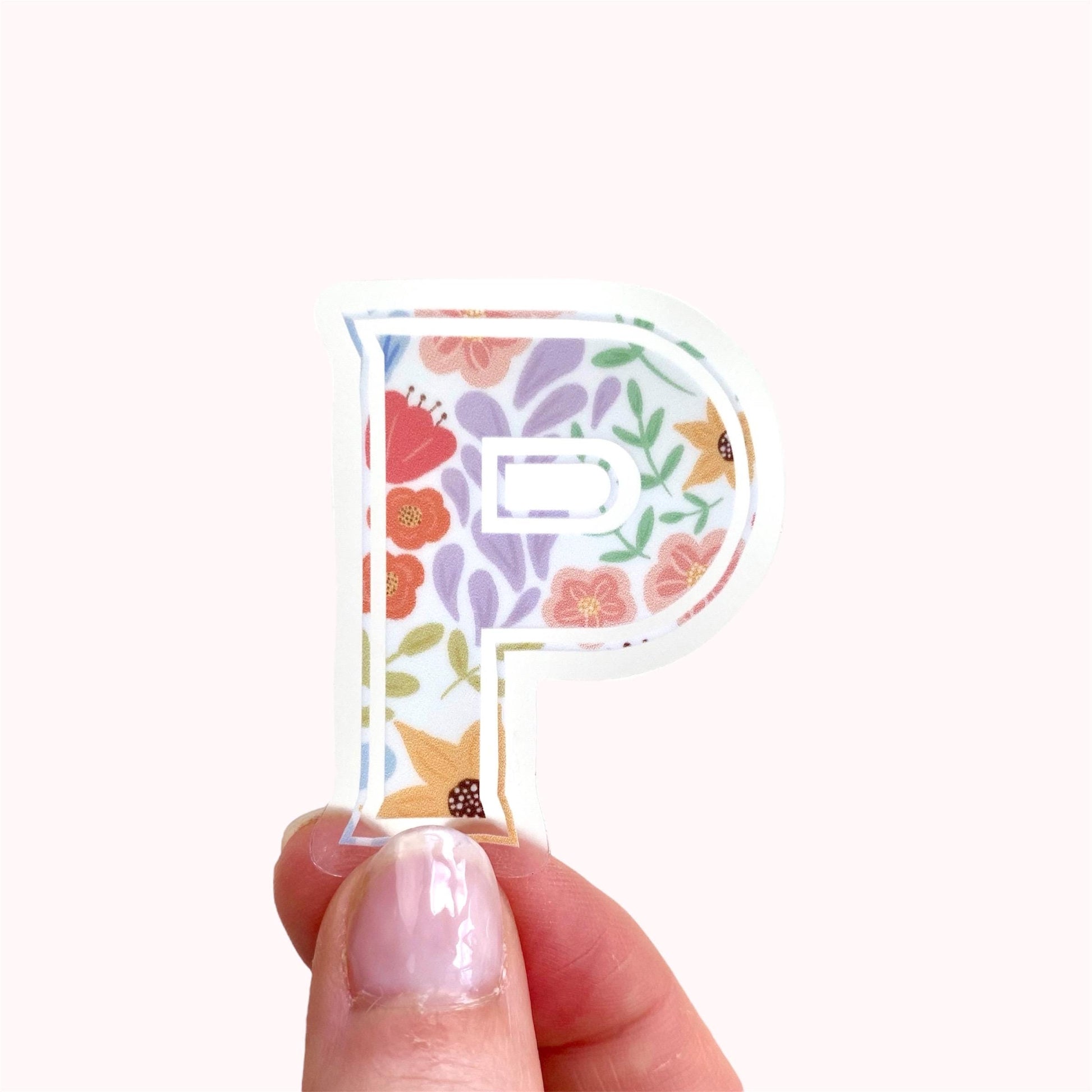 Floral letter 'P' sticker held between fingers on a white background