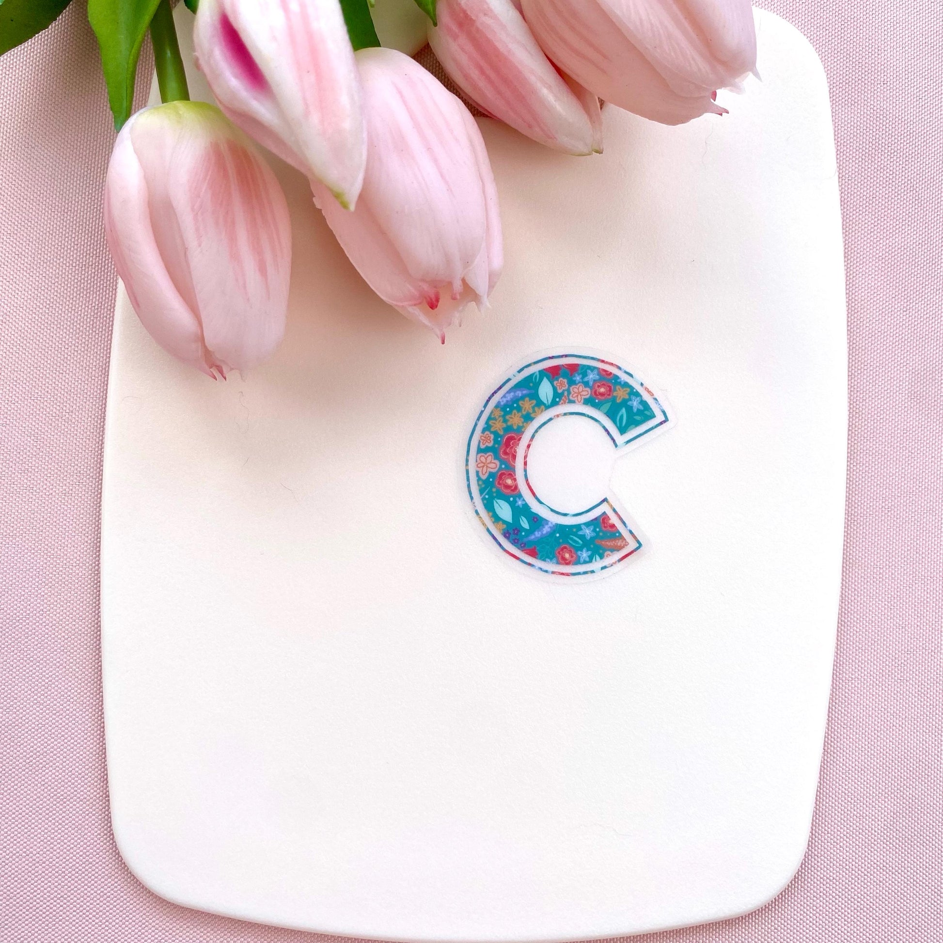 Floral letter 'C' sticker on a white board with pink tulips against a pink background