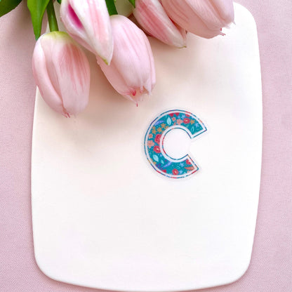 Floral letter 'C' sticker on a white board with pink tulips against a pink background