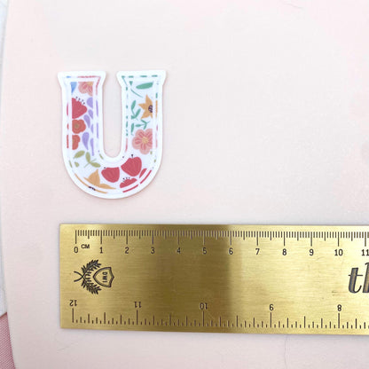 Floral letter 'U' sticker on a pink background with a ruler for scale.