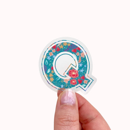 Sticker with letter 'Q' with floral design held by a hand on a white background