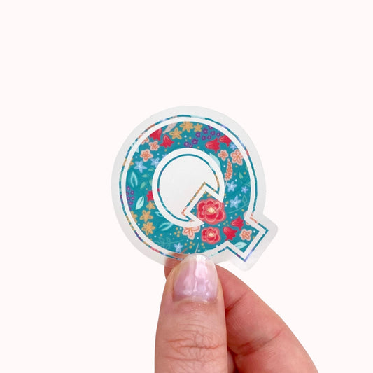 Sticker with letter 'Q' with floral design held by a hand on a white background