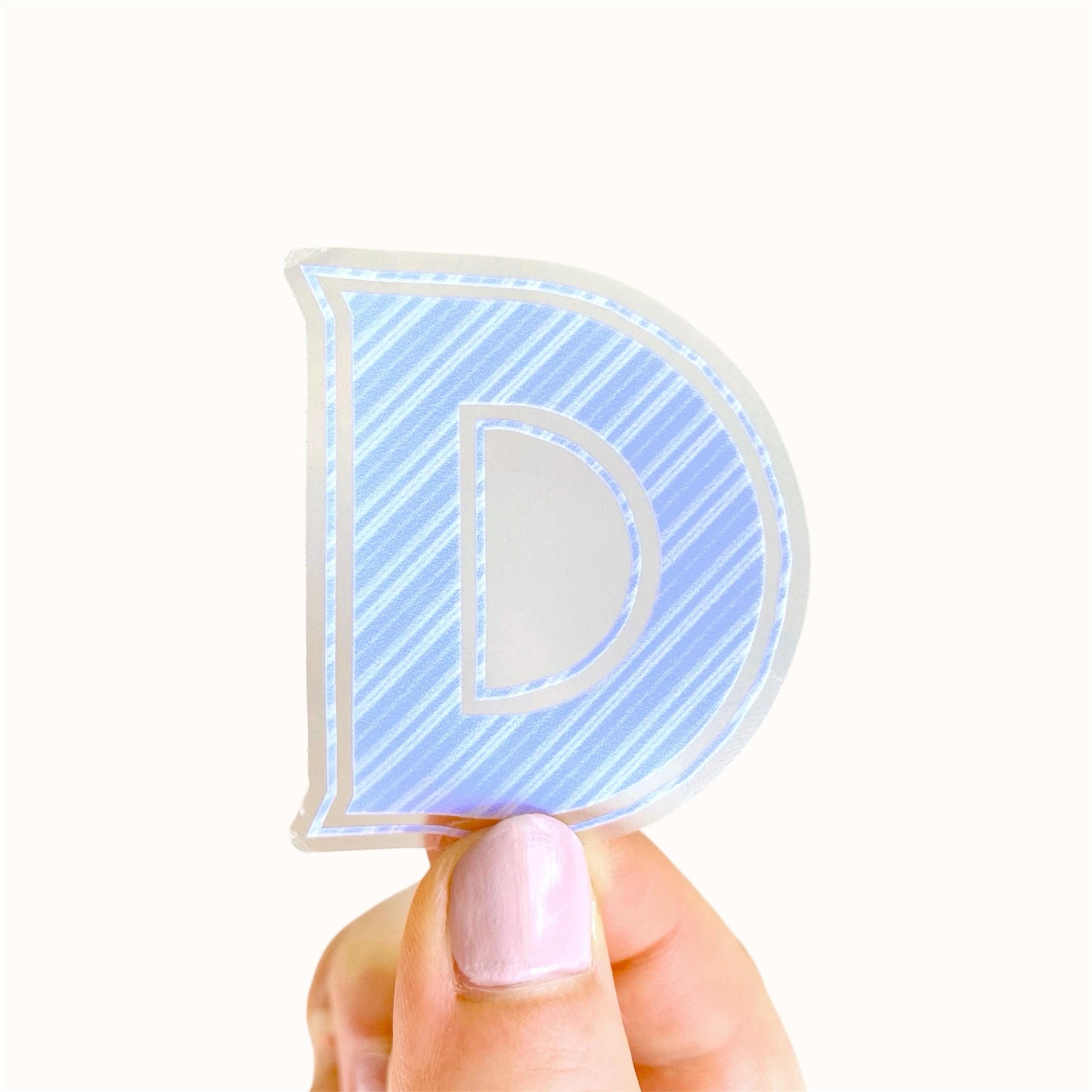 Hand holding a blue striped letter 'D' sticker against a white background