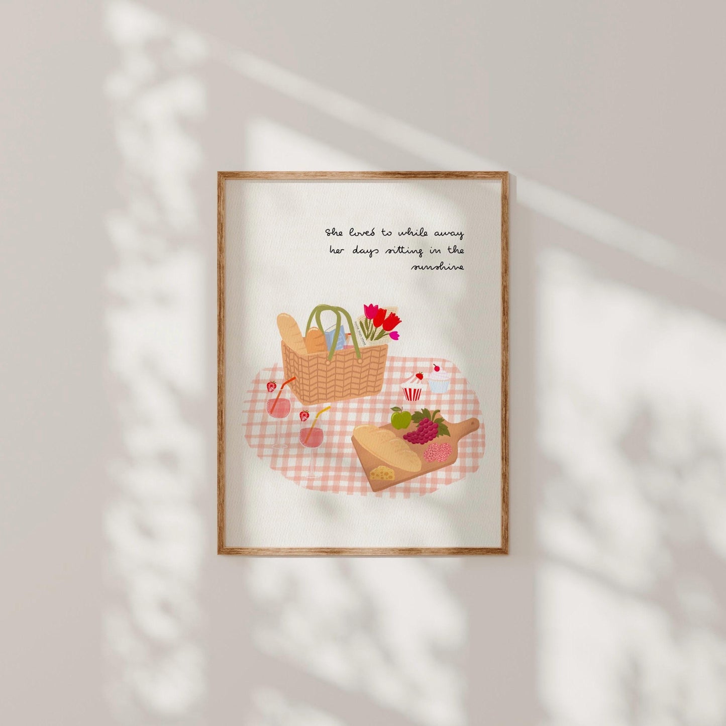 Framed artwork of a picnic scene with a basket, cutting board, and flowers on a checkered tablecloth.