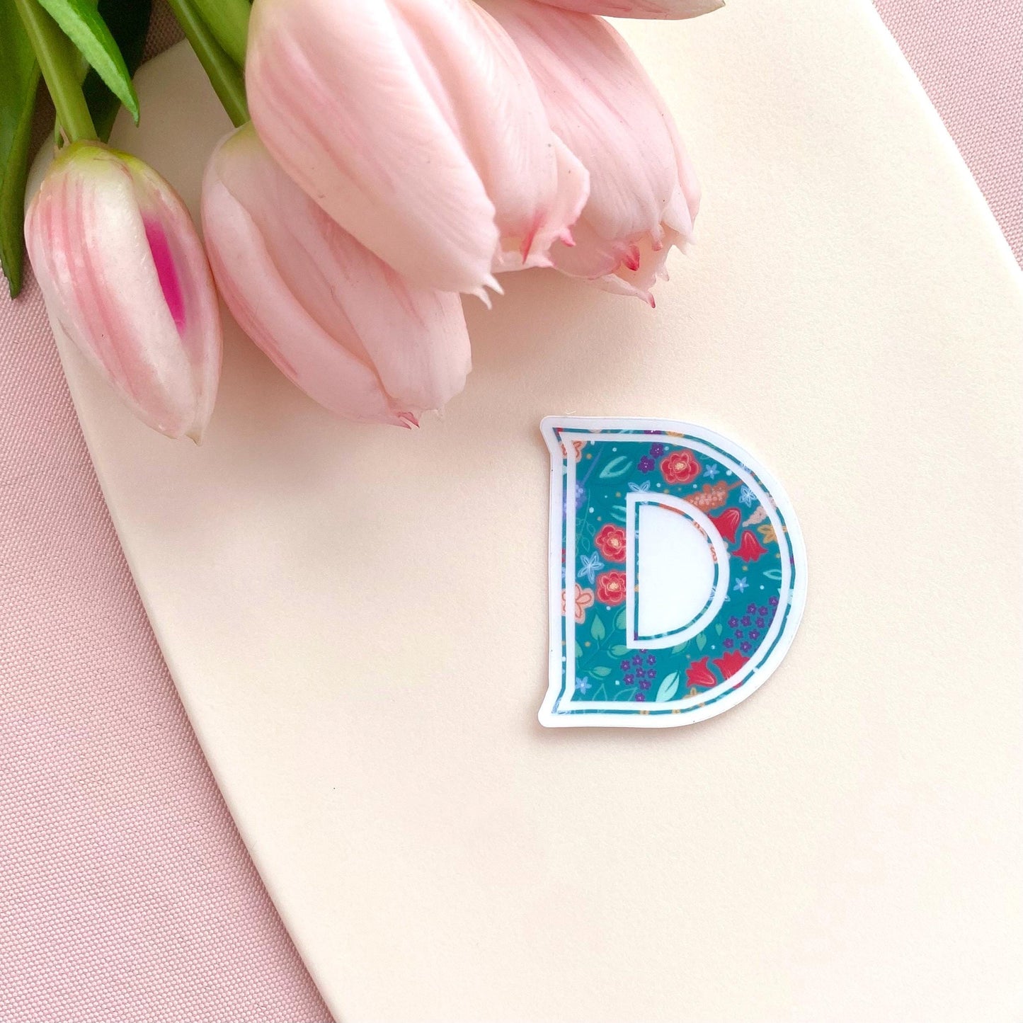 Floral letter 'D' sticker on a pink surface with tulips