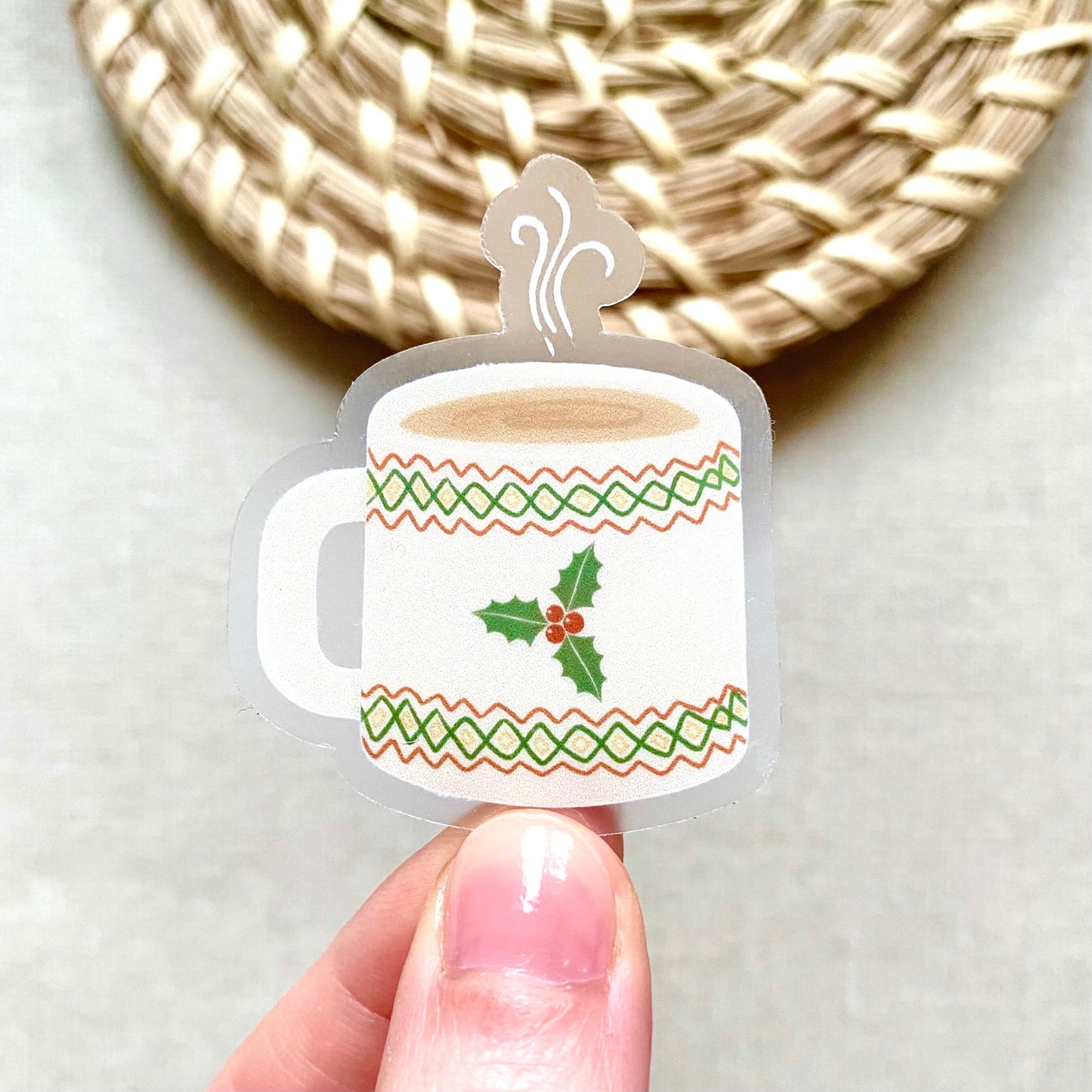 Decorative Christmas mug sticker held by a hand with a woven mat in the background
