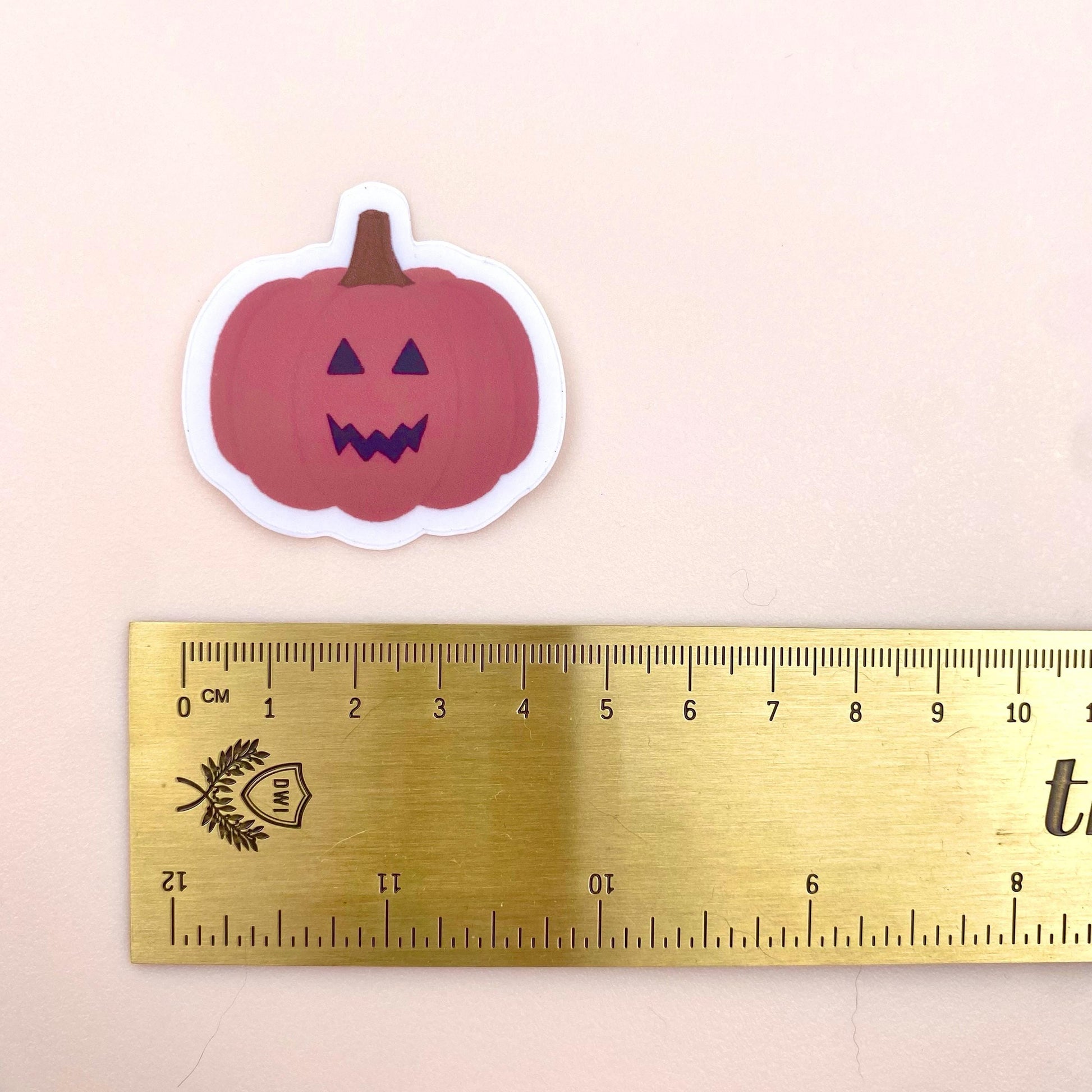 Pink pumpkin sticker with a ruler for scale on a beige background