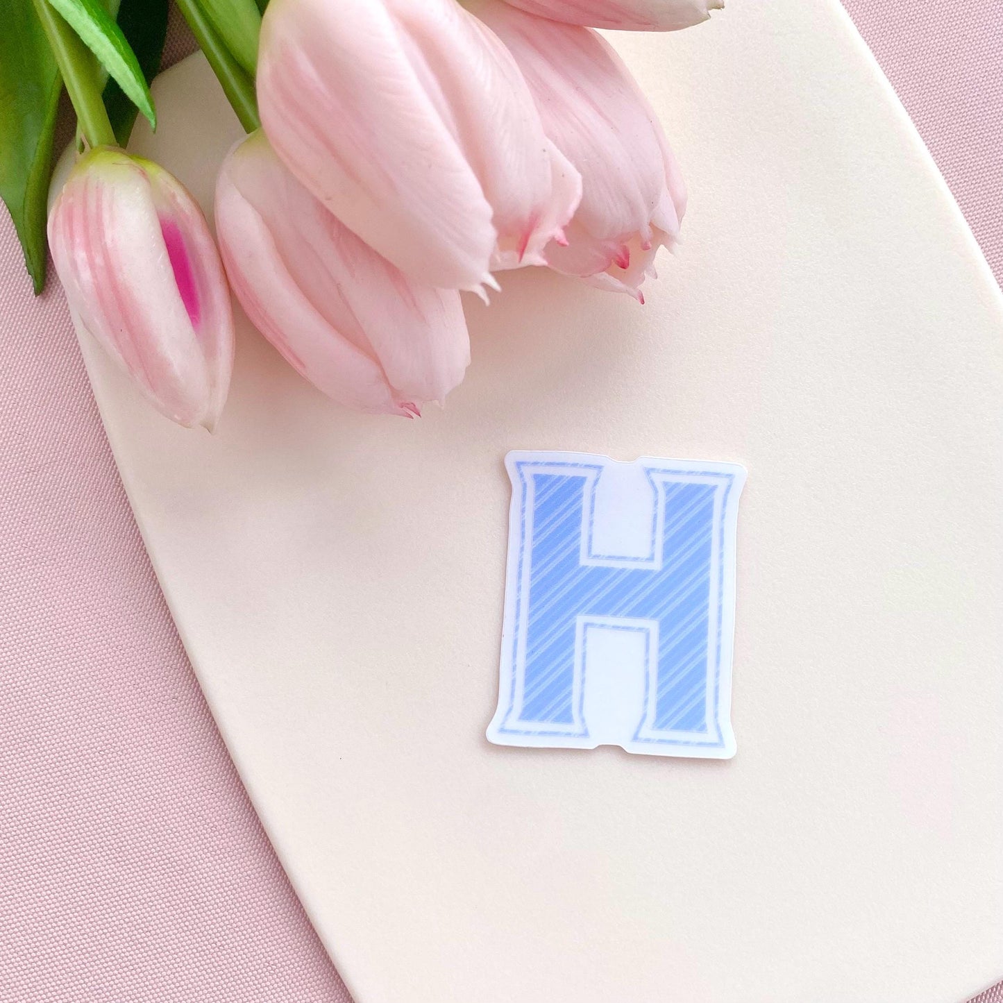 Blue striped letter 'H' sticker and pink tulips on a pink background