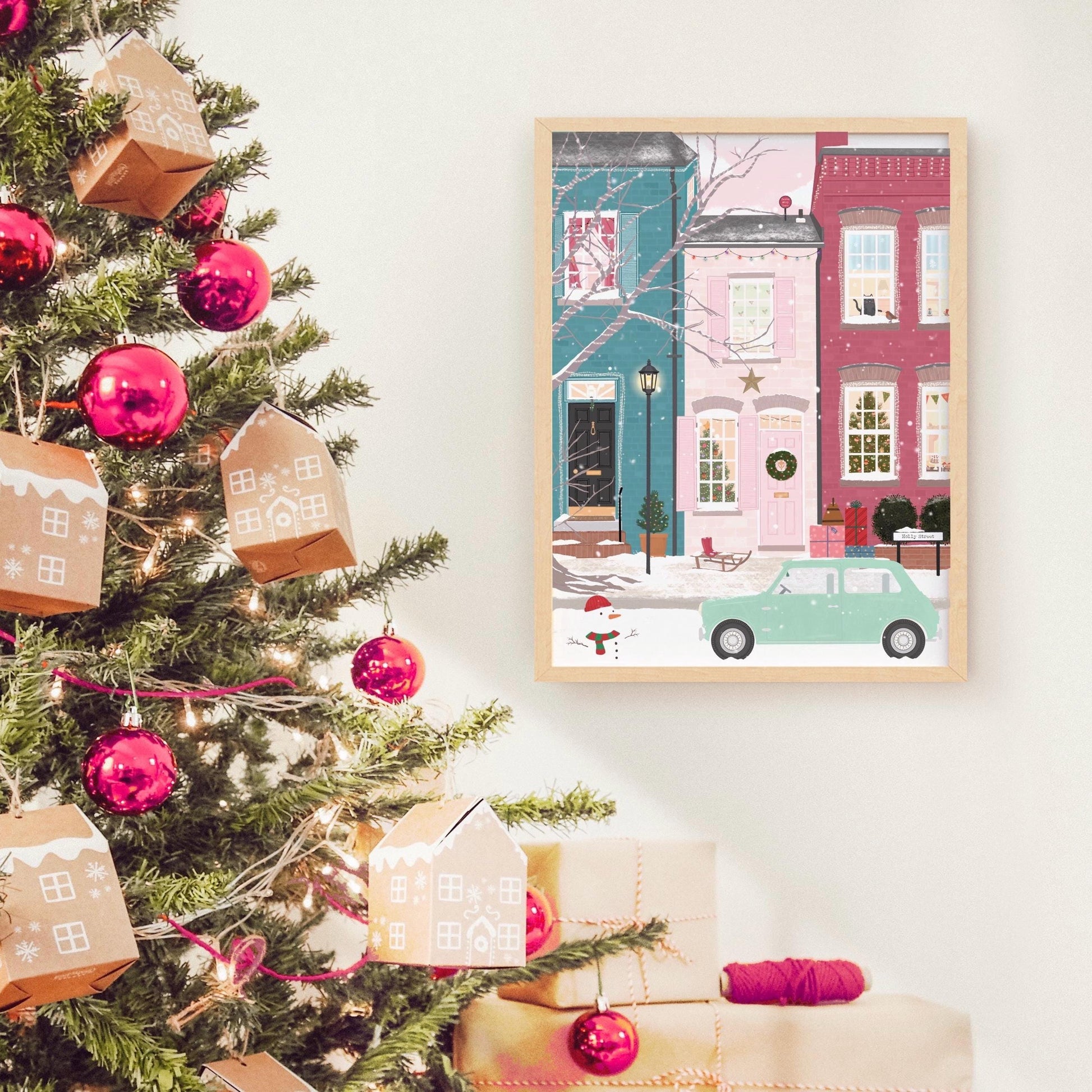 Decorated Christmas tree with presents and a framed artwork of a snowy street scene.