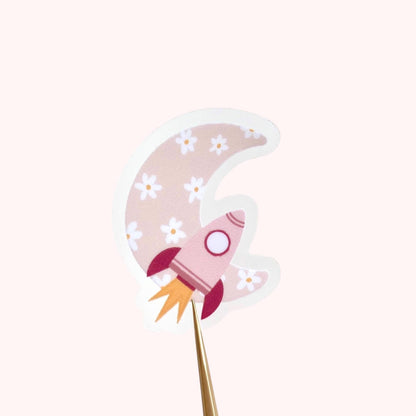 Decorative sticker with pink rocket and floral moon design on a white background