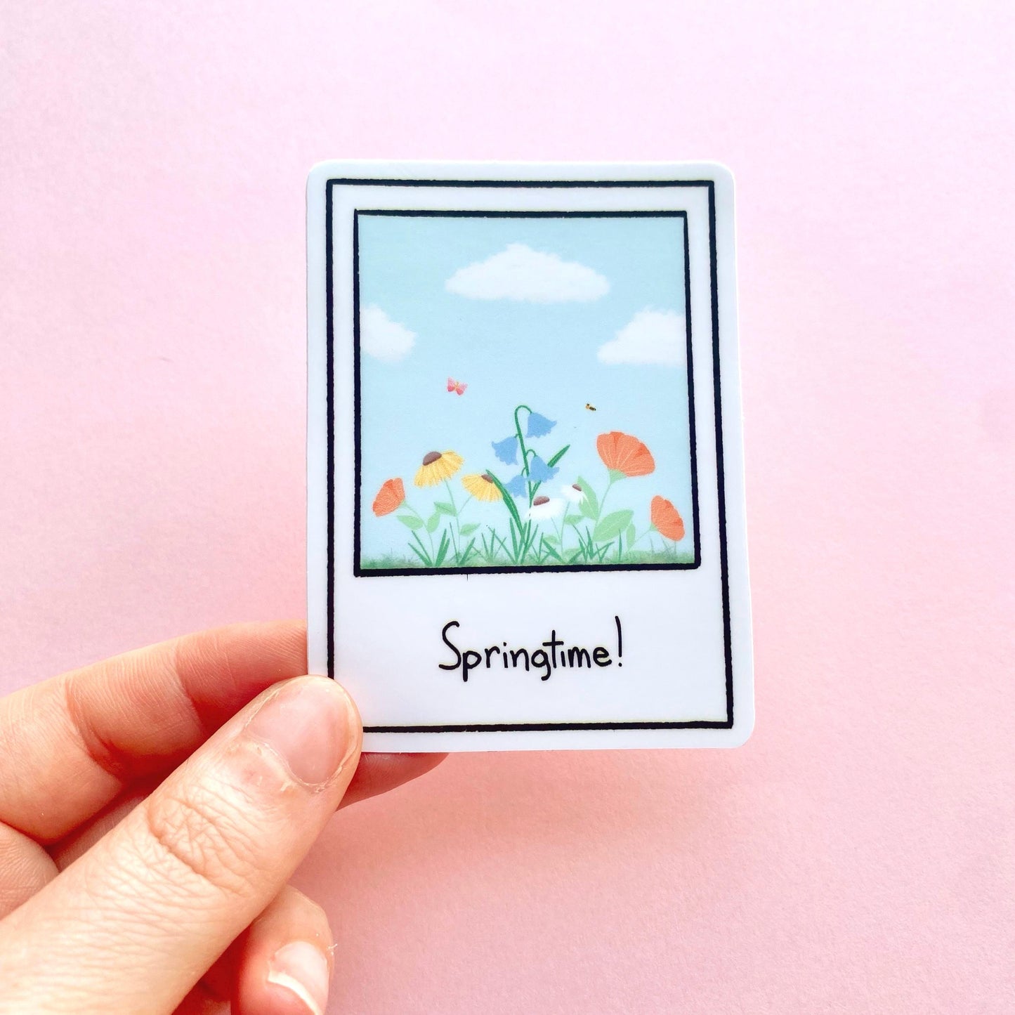 Sticker with a springtime polaroid design held by a hand on a pink background