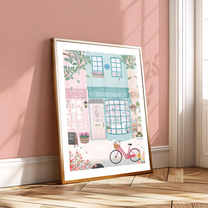 Framed illustration of a quaint street scene with a bookshop, pink bicycle, and flowers on a wooden floor.