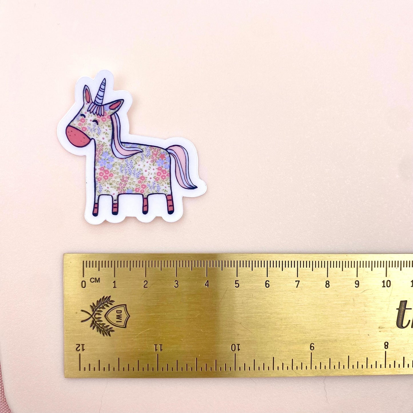 Floral unicorn sticker next to a ruler on a beige background