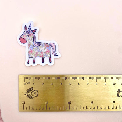 Floral unicorn sticker next to a ruler on a beige background