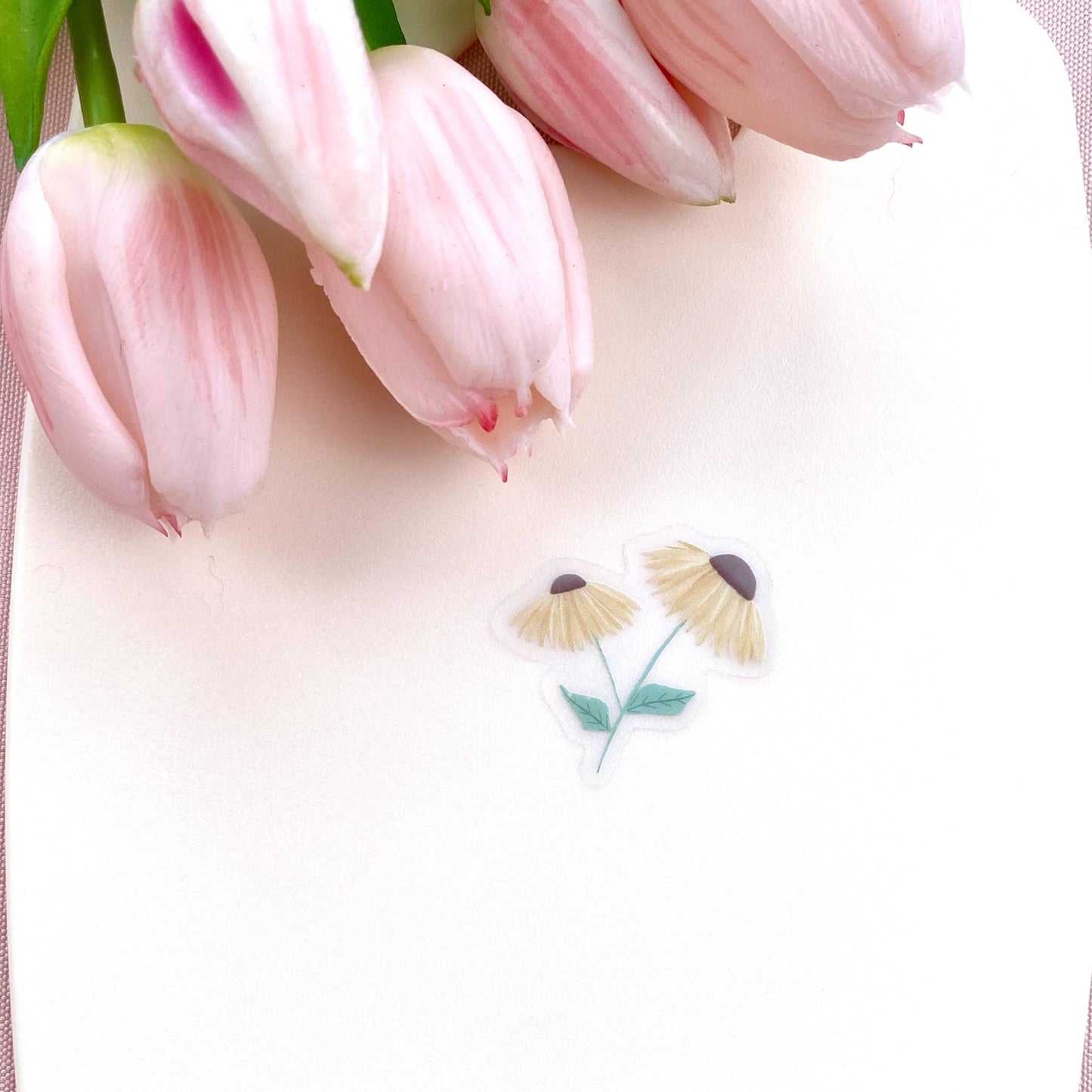 A sticker with 2 yellow daisies against a cream background with pink tulips.