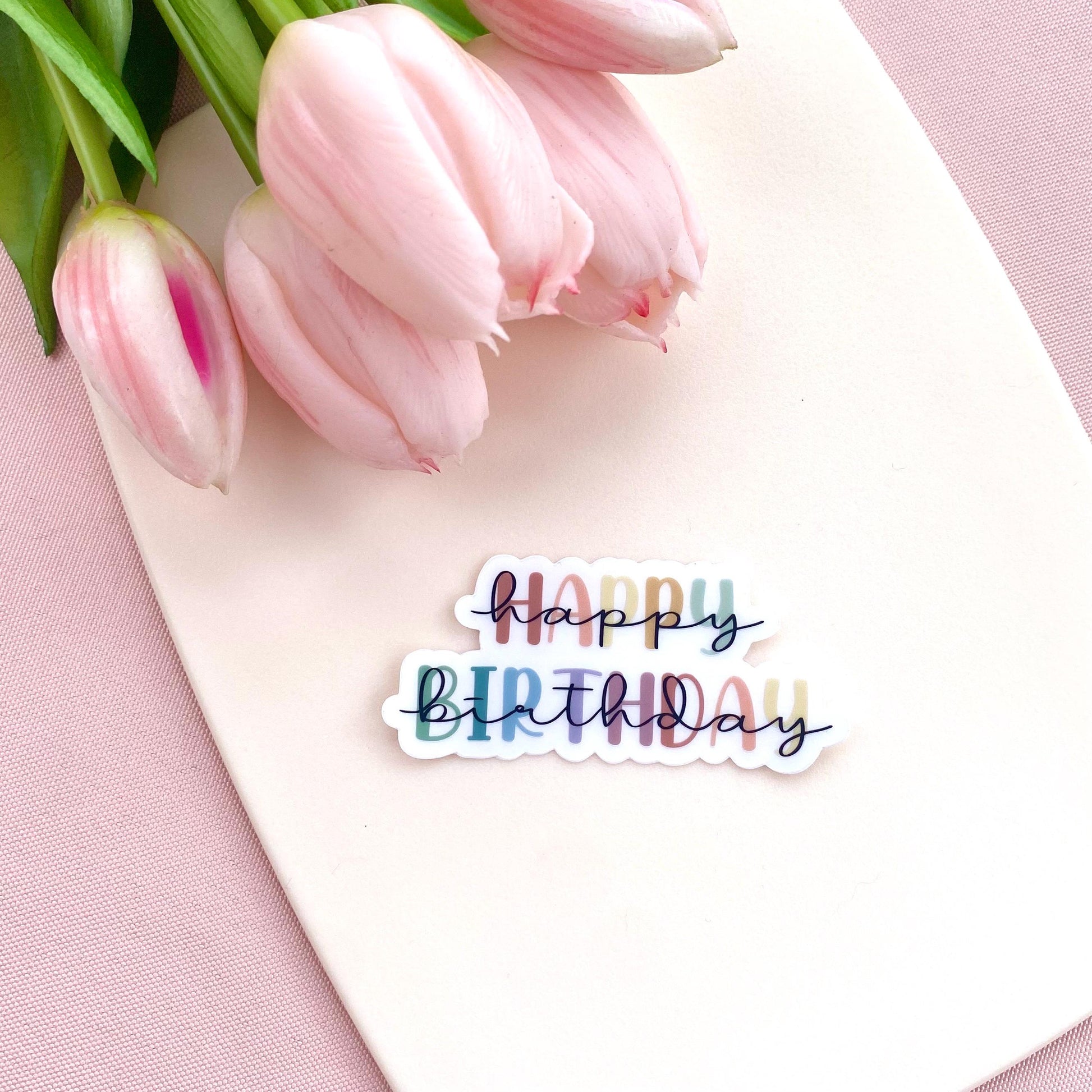Colourful transparent 'Happy Birthday' sticker on a white background with pink tulips