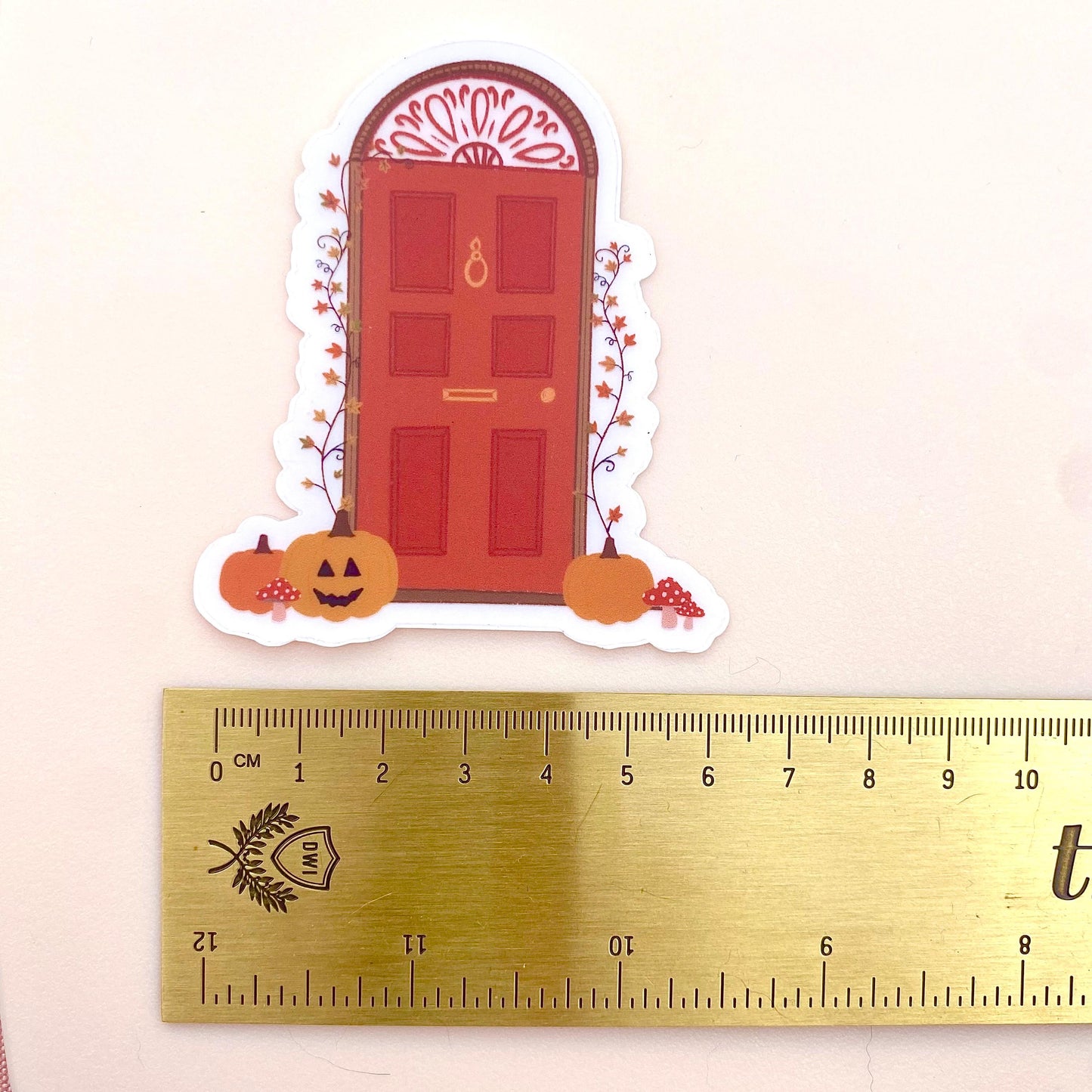 Decorative Halloween door sticker with pumpkins and a red door on a white background with a gold ruler for scale..
